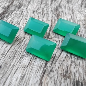 May include: Five emerald green gemstone cabochons in a rectangular shape, displayed on a wooden surface.
