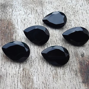 May include: Five black pear-shaped gemstones on a wooden surface.