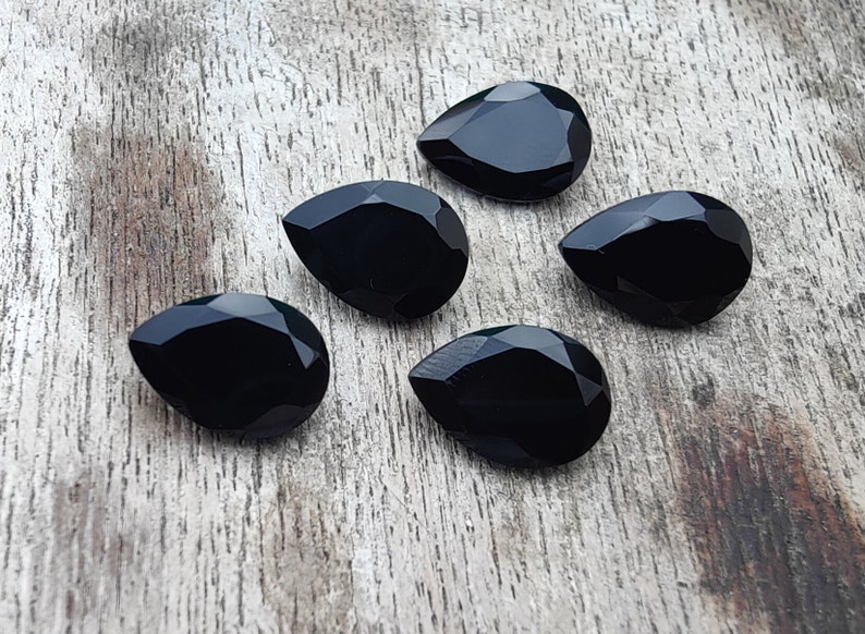 May include: Five black pear-shaped gemstones on a wooden surface.