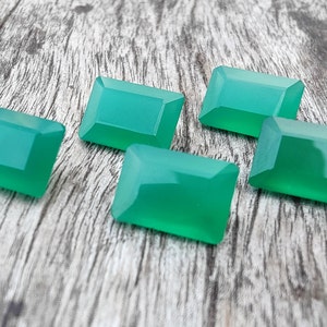 May include: Five green gemstone cabochons in a rectangular shape, with a smooth, polished surface. The stones are arranged on a wooden surface.