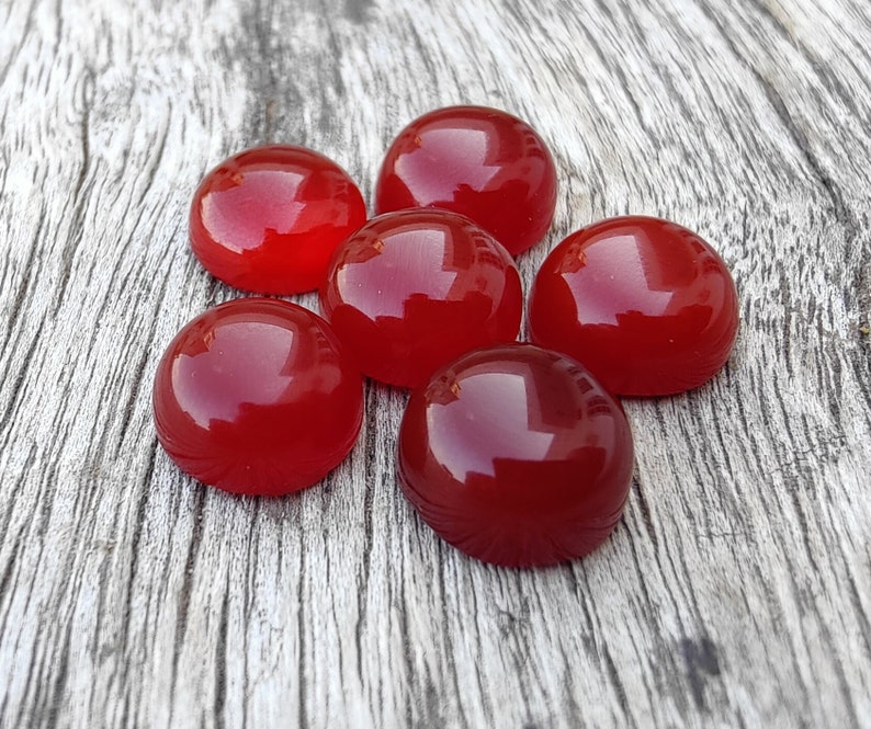 K&ouml;nnte beinhalten: Sechs runde, rote Cabochonsteine auf einem Holzgrund.