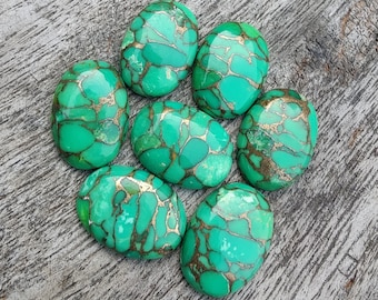 May include: Seven oval-shaped turquoise cabochons with a green and gold marbled pattern. The stones are arranged in a circle on a wooden surface.