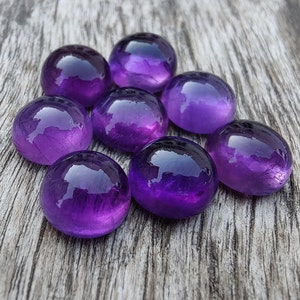 May include: Eight round, purple amethyst gemstones on a wooden surface.