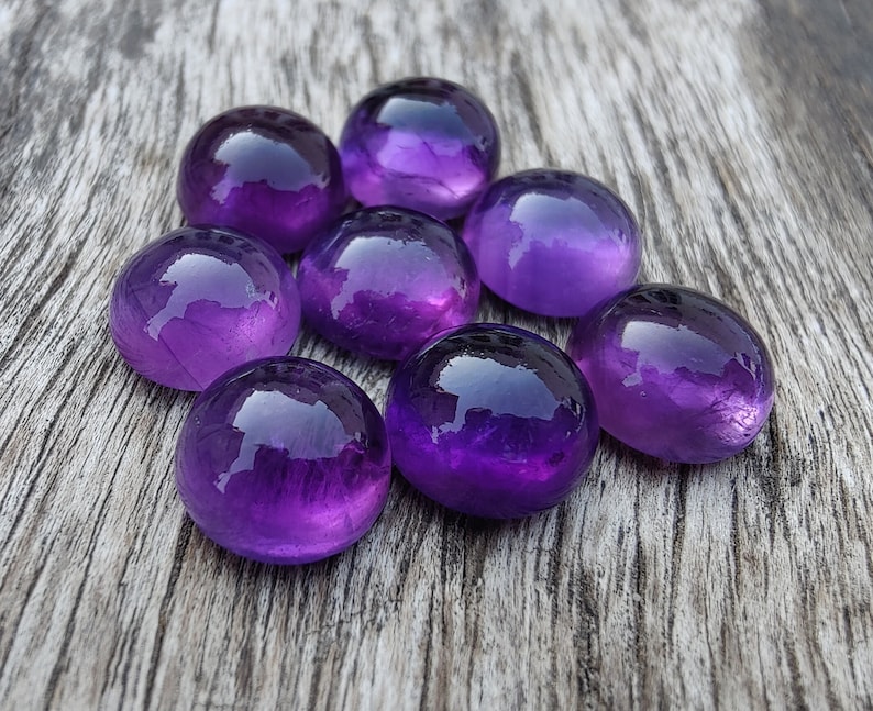 May include: Eight round, purple amethyst gemstones on a wooden surface.