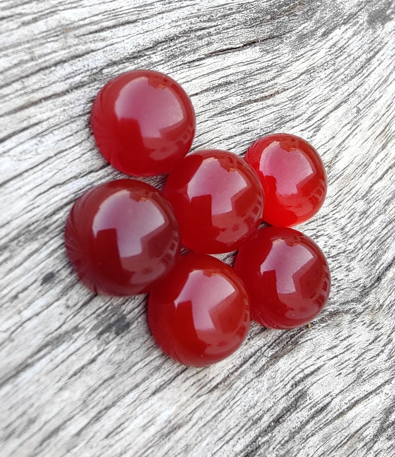 K&ouml;nnte beinhalten: Sechs runde, rote Cabochonsteine auf einem Holzgrund.