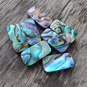 Puede incluir: Una colección de siete azulejos de concha de abulón iridiscente en varios tonos de azul, verde y morado. Los azulejos son rectangulares y tienen una superficie lisa y pulida.