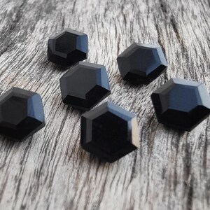 May include: Six black, faceted, hexagonal buttons on a wooden surface.