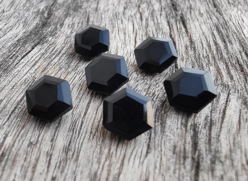 May include: Six black, faceted, hexagonal buttons on a wooden surface.