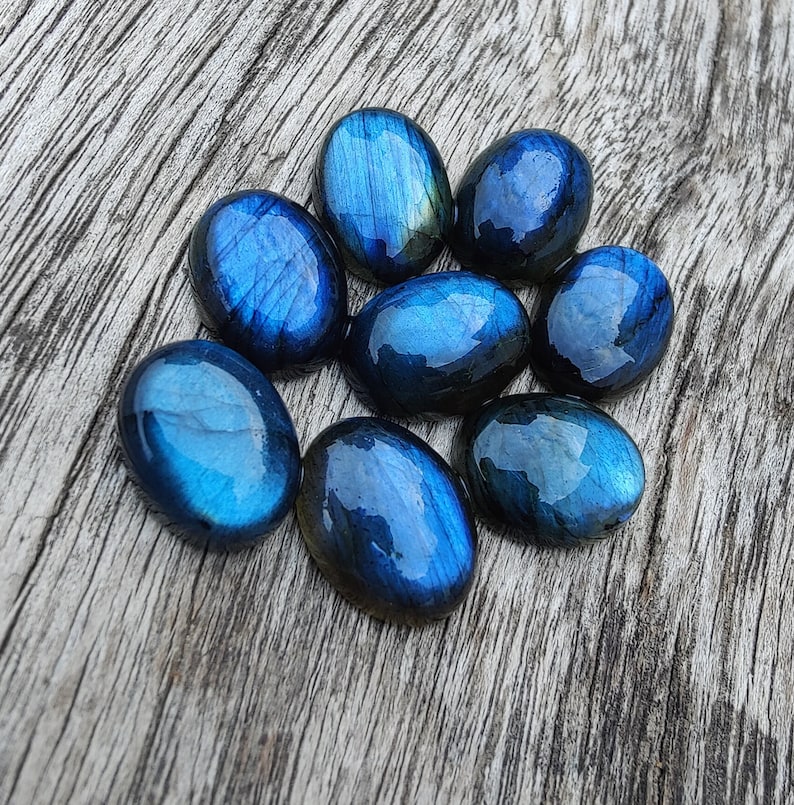 May include: A collection of eight oval-shaped labradorite stones, each with a deep blue and iridescent sheen. The stones are arranged in a circle on a wooden surface.