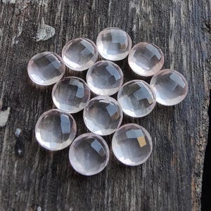 May include: A collection of 12 pale pink rose quartz cabochons, each with a smooth, rounded surface and a slightly translucent appearance.