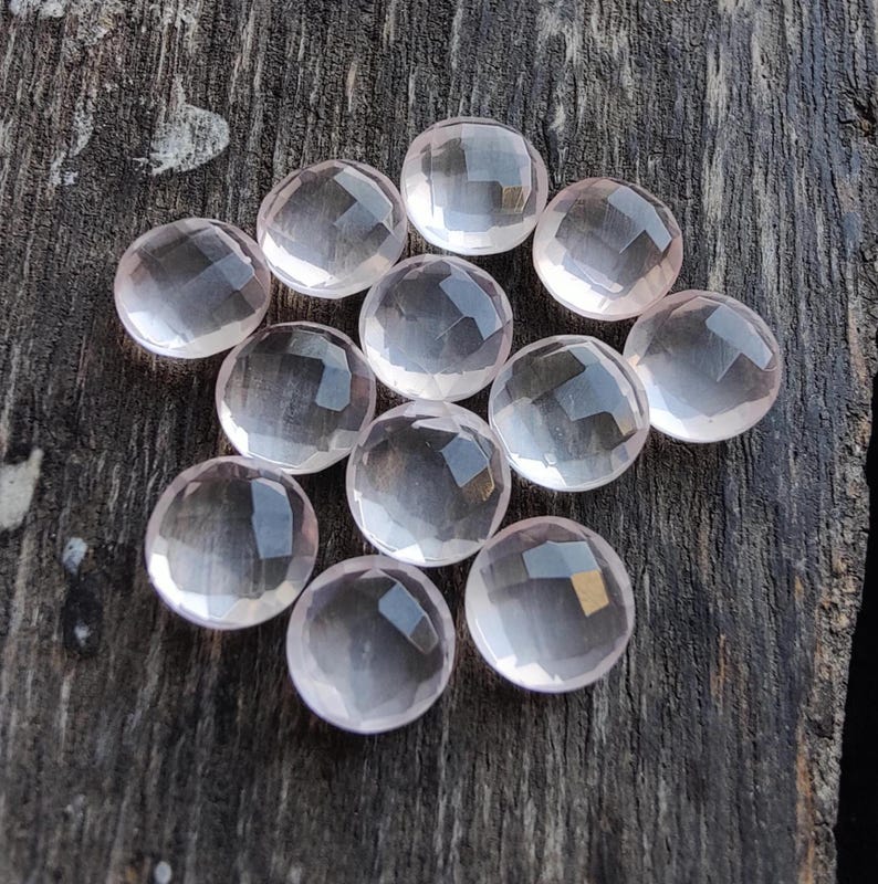 May include: A collection of 12 pale pink rose quartz cabochons, each with a smooth, rounded surface and a slightly translucent appearance.