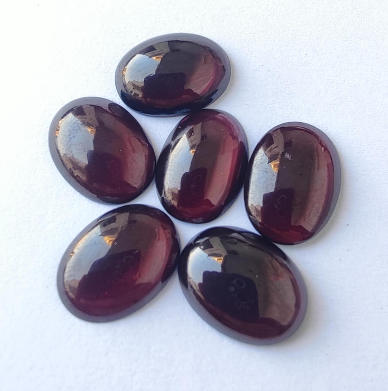 Puede incluir: Seis piedras preciosas ovaladas de color p&uacute;rpura oscuro con un acabado brillante. Las piedras est&aacute;n dispuestas en un racimo.
