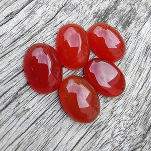 Op de afbeelding: Vijf ovale carneol edelstenen in tinten van rood en oranje. De stenen zijn glad en gepolijst, met een glanzende afwerking.