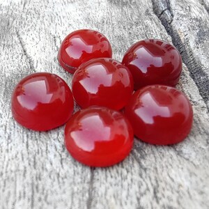 K&ouml;nnte beinhalten: Sechs runde, rote Karneol-Cabochons, poliert und glatt, auf einer Holzoberfl&auml;che angeordnet.