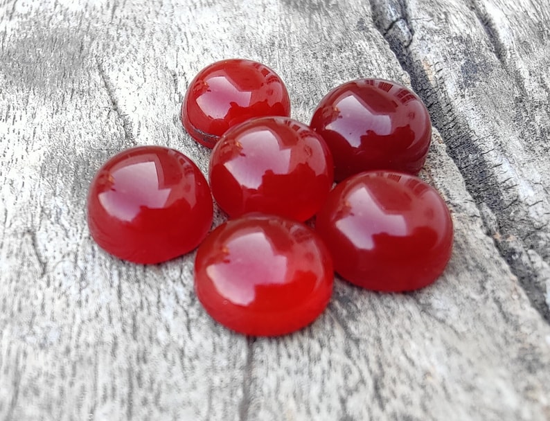 K&ouml;nnte beinhalten: Sechs runde, rote Karneol-Cabochons, poliert und glatt, auf einer Holzoberfl&auml;che angeordnet.