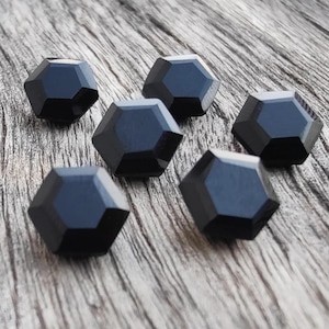 May include: Six black faceted glass beads, each with a unique geometric shape, arranged on a wooden surface.