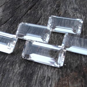 May include: Five clear, rectangular, faceted, quartz crystals on a dark wood surface.