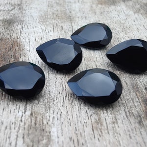 May include: Five black teardrop-shaped gemstones on a wooden surface.