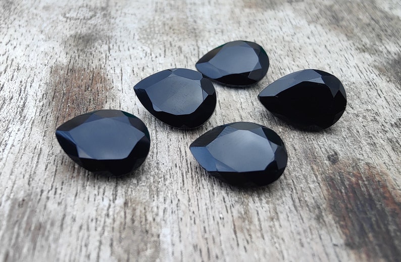 May include: Five black teardrop-shaped gemstones on a wooden surface.