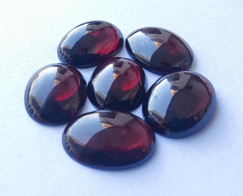 Puede incluir: Seis piedras preciosas ovaladas de color rojo oscuro con un acabado brillante.