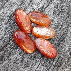 K&ouml;nnte beinhalten: F&uuml;nf glatte, ovale Sunstone-Edelsteine in Orange- und Rott&ouml;nen mit einem schimmernden, irisierenden Finish.