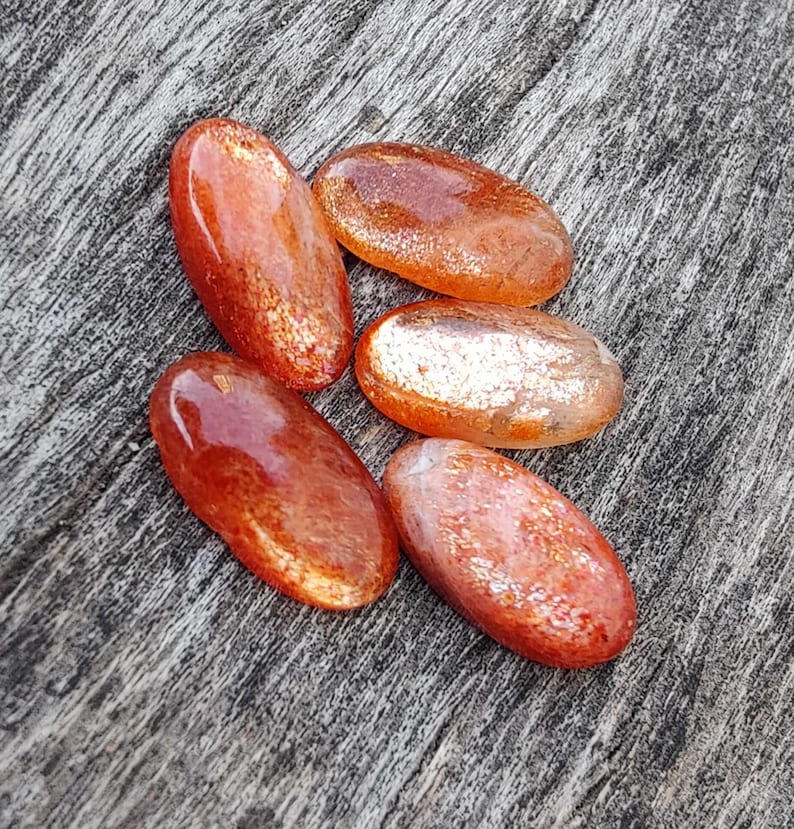 K&ouml;nnte beinhalten: F&uuml;nf glatte, ovale Sunstone-Edelsteine in Orange- und Rott&ouml;nen mit einem schimmernden, irisierenden Finish.