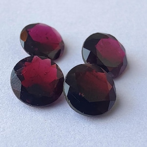 May include: Four round, faceted gemstones with a deep red color. The gemstones have a dark, almost black, appearance in some areas.