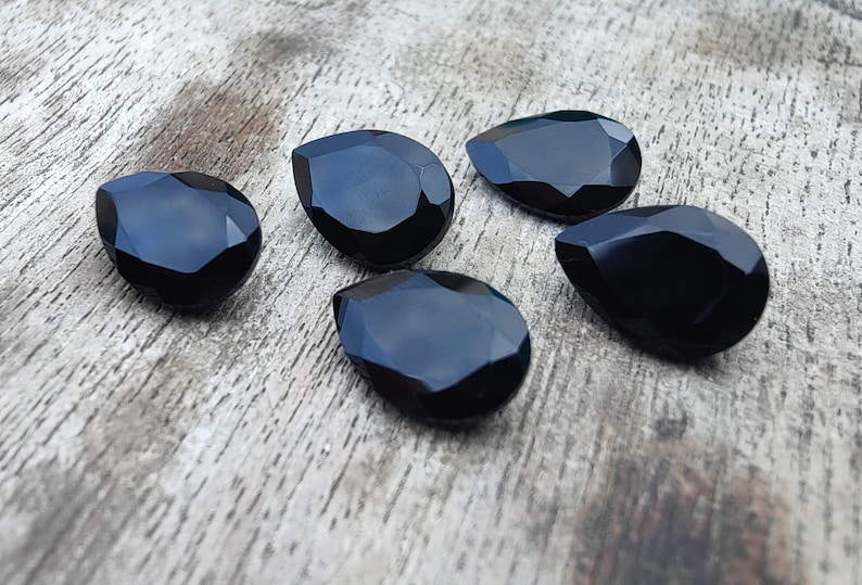 May include: Five black teardrop-shaped crystal beads. The beads are faceted and have a glossy finish.