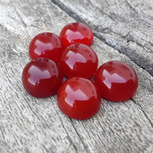 K&ouml;nnte beinhalten: Sechs runde, rote Edelsteinkabochons, wahrscheinlich Karneol, auf einer Holzoberfl&auml;che.
