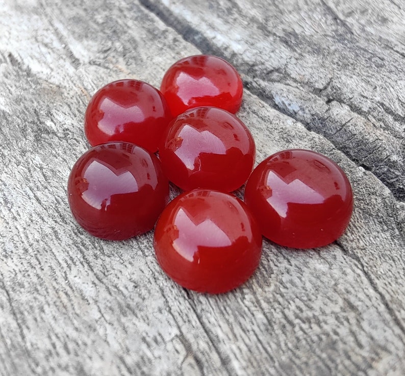 K&ouml;nnte beinhalten: Sechs runde, rote Edelsteinkabochons, wahrscheinlich Karneol, auf einer Holzoberfl&auml;che.