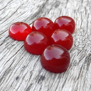 K&ouml;nnte beinhalten: Sechs rote Cabochon-Edelsteine auf einer Holzoberfl&auml;che. Die Edelsteine sind rund und haben eine glatte, polierte Oberfl&auml;che.
