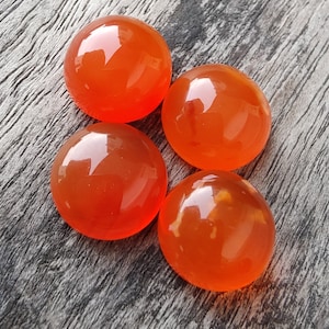 Puede incluir: Cuatro piedras redondas de cornalina naranja sobre una superficie de madera.