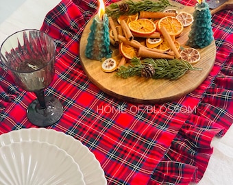 Pode incluir: Um corredor de mesa vermelho e preto xadrez com uma borda franjada. O corredor é decorado com duas velas de árvore de Natal turquesa, paus de canela e fatias de laranja secas. O texto "HOME OF BLOSSOM" é visível no corredor.