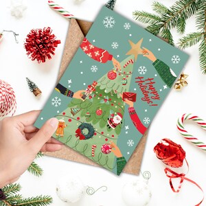 May include: A green Christmas card with a cartoon illustration of a Christmas tree decorated with ornaments, candy canes, and a star on top.  Multiple hands are decorating the tree. The text "Happy Holidays!" is written on the card.