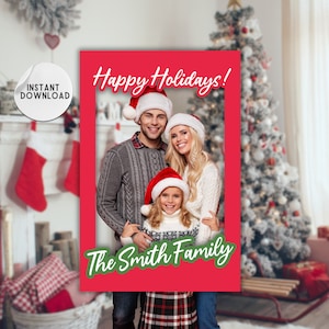 May include: A red photo booth frame with a white border and the text "Happy Holidays!" in red. The frame has a green border with the text "The Smith Family" in white. A family of three is standing in the frame wearing Santa hats.