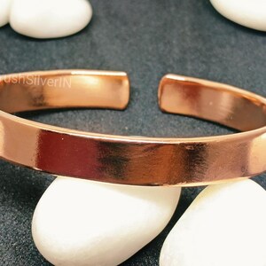 Peut inclure: Un bracelet en cuivre brillant avec une finition lisse et polie. Le bracelet est ouvert aux deux extr&eacute;mit&eacute;s et pr&eacute;sente un design simple et minimaliste.