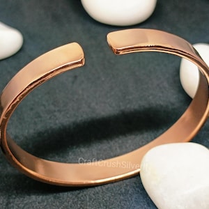 Peut inclure: Un bracelet jonc simple en cuivre. Le bracelet est ouvert et a une finition lisse et polie.