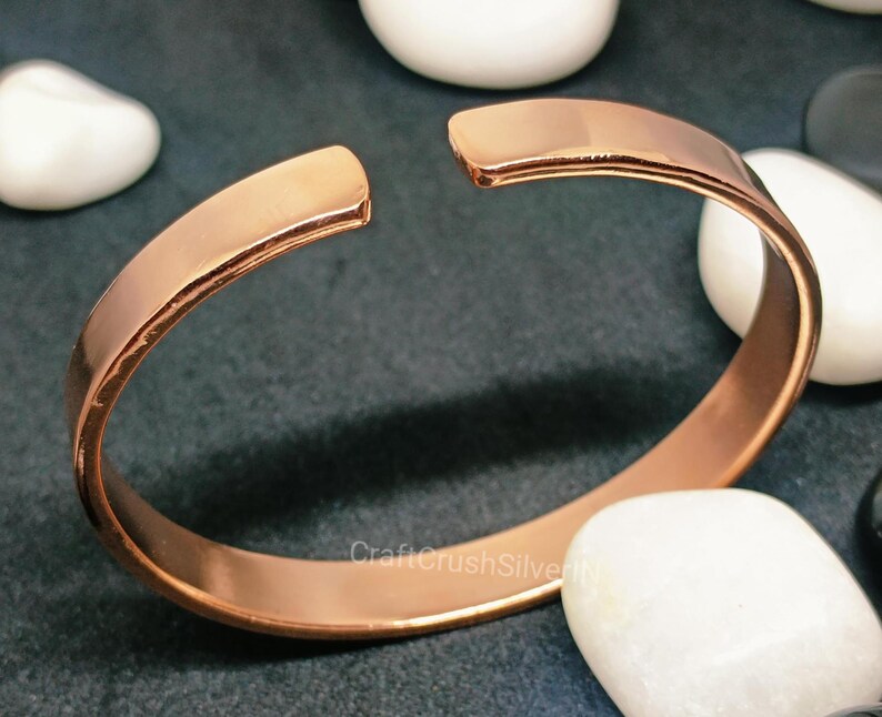 Peut inclure: Un bracelet jonc simple en cuivre. Le bracelet est ouvert et a une finition lisse et polie.