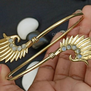 May include: Gold-tone bangle bracelet with two wing-shaped charms. Each charm has a row of clear moonstone-like stones.
