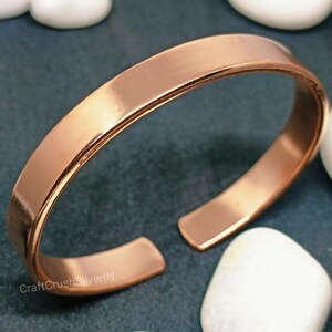Peut inclure: Un bracelet en cuivre simple avec une finition lisse et polie. Le bracelet est ouvert aux deux extr&eacute;mit&eacute;s et pr&eacute;sente une l&eacute;g&egrave;re courbure.