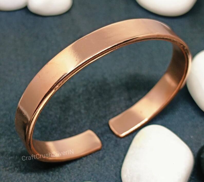 Peut inclure: Un bracelet en cuivre simple avec une finition lisse et polie. Le bracelet est ouvert aux deux extr&eacute;mit&eacute;s et pr&eacute;sente une l&eacute;g&egrave;re courbure.