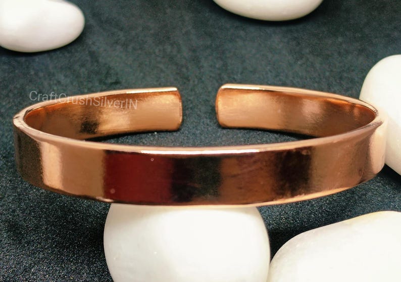 Peut inclure: Un bracelet en cuivre brillant avec une finition lisse et polie. Le bracelet est ouvert aux deux extr&eacute;mit&eacute;s et pr&eacute;sente un design simple et minimaliste.
