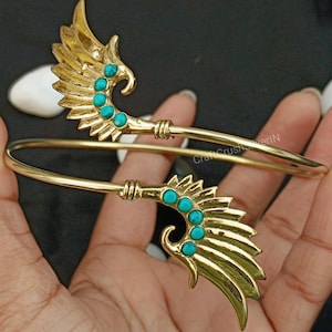 May include: Gold-toned bangle bracelet with two wing-shaped charms. Each charm is decorated with turquoise-colored stones.