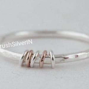May include: A silver ring with a hammered finish and a band of twisted silver and rose gold wire.