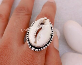 May include: A silver ring with a white cowrie shell set in the center. The ring is decorated with small silver beads around the edge.