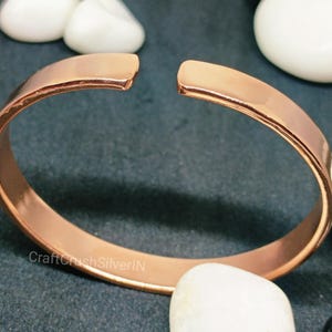 Peut inclure: Un bracelet jonc en cuivre simple avec une finition lisse et polie. Le bracelet est ouvert aux deux extr&eacute;mit&eacute;s et pr&eacute;sente un l&eacute;ger espace &agrave; l'endroit o&ugrave; les extr&eacute;mit&eacute;s se rejoignent.