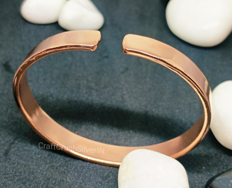 Peut inclure: Un bracelet jonc en cuivre simple avec une finition lisse et polie. Le bracelet est ouvert aux deux extr&eacute;mit&eacute;s et pr&eacute;sente un l&eacute;ger espace &agrave; l'endroit o&ugrave; les extr&eacute;mit&eacute;s se rejoignent.