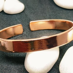 Peut inclure: Un bracelet en cuivre simple avec une finition lisse et polie. Le bracelet est ouvert aux deux extr&eacute;mit&eacute;s et a un bord l&eacute;g&egrave;rement arrondi.