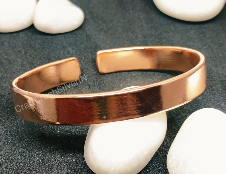Peut inclure: Un bracelet en cuivre simple avec une finition lisse et polie. Le bracelet est ouvert aux deux extr&eacute;mit&eacute;s et a un bord l&eacute;g&egrave;rement arrondi.