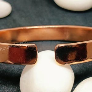 Peut inclure: Un bracelet en cuivre avec un espace sur un c&ocirc;t&eacute;. Le bracelet est brillant et a une surface lisse. Le texte "CraftCrushSilverIN" est visible sur le bracelet.